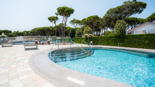 Piscina exterior con bancos y árboles en Camping Village Cavallino, un parque vacacional en Veneto, Italia.