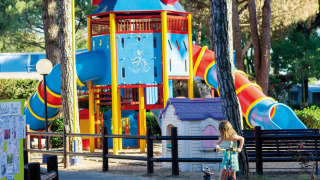 Colorido parque infantil en Camping Village Cavallino, Véneto, Italia, con toboganes y una niña en patinete.