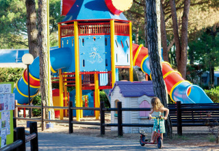 Kleurrijke speeltuin bij Camping Village Cavallino, Veneto, Italië, met glijbanen en kind op step.