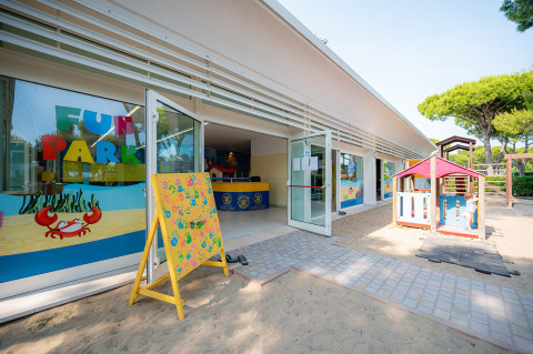 Zona de juegos infantiles al aire libre en Camping Village Cavallino, Véneto, Italia, con juguetes y carteles.