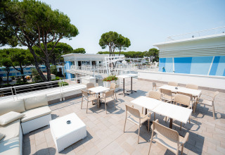 Tagterrasse med borde, stole og loungemøbler på Camping Village Cavallino i Veneto, Italien om sommeren.