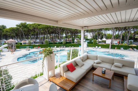 Udsigt over poolområdet fra en overdækket terrasse med loungemøbler på Camping Village Cavallino, Veneto, Italien.