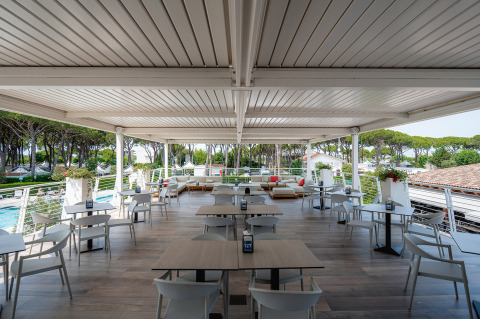 Terraza exterior techada con mesas y sillas en Camping Village Cavallino, un parque vacacional en Véneto, Italia.