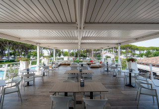 Udendørs terrasseområde med borde og stole på Camping Village Cavallino i Veneto, Italien, omgivet af grønne træer.