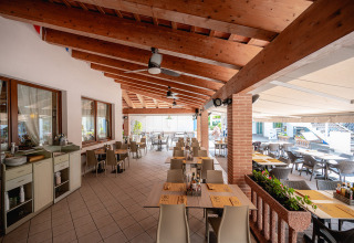 Outdoor dining area at Camping Village Cavallino, Veneto, Italy, with tables, chairs and wooden beams.