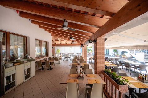 Zona de comedor al aire libre en Camping Village Cavallino, Véneto, Italia, con mesas y vigas de madera.