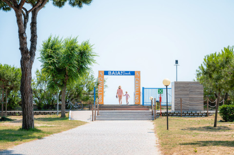 Ingresso alla Baia Beach del Camping Village Cavallino, con due persone che camminano verso la spiaggia in Veneto.