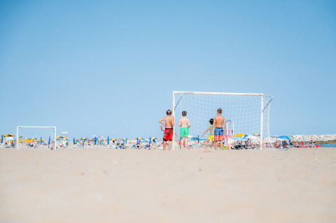 Bambini giocano a calcio sulla spiaggia al Camping Village Cavallino in Veneto, Italia, tra gli ombrelloni.