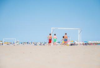 Niños juegan al fútbol playa en Camping Village Cavallino, Véneto, Italia, con sombrillas al fondo.