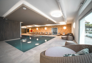 Piscina coperta con lettini e sedute in rattan al Camping Village Cavallino, Veneto, Italia.