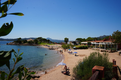 Plage du Centro Vacanze Isuledda en Sardaigne, Italie, avec vacanciers, parasols et eau claire sous un ciel bleu.