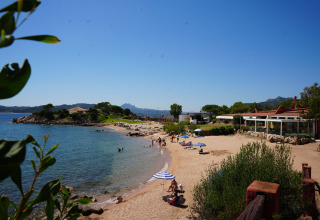 Strandbillede fra Centro Vacanze Isuledda feriested i Sardinien, Italien, med solbadende gæster og klart vand.