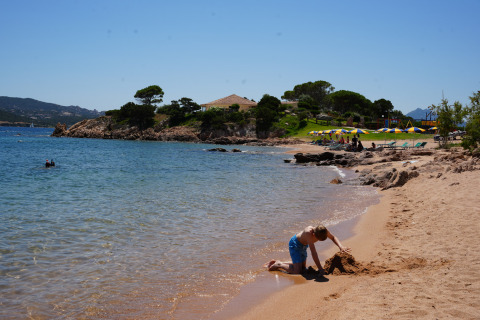 Jongen bouwt een zandkasteel op het strand bij Centro Vacanze Isuledda, Sardinië, met parasols verderop.