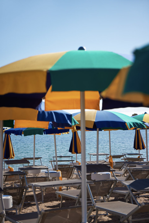 Beach chairs and colorful umbrellas by the sea at Centro Vacanze Isuledda, a holiday park in Sardinia, Italy.