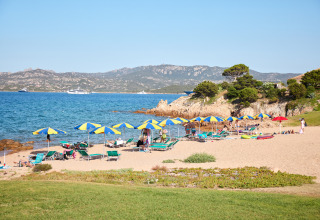 Strandscene med parasoller og liggestole ved Centro Vacanze Isuledda feriepark på Sardinien, Italien.
