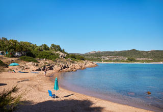 Solrig strand ved Centro Vacanze Isuledda, Sardinien, Italien, med blå himmel og klart vand.