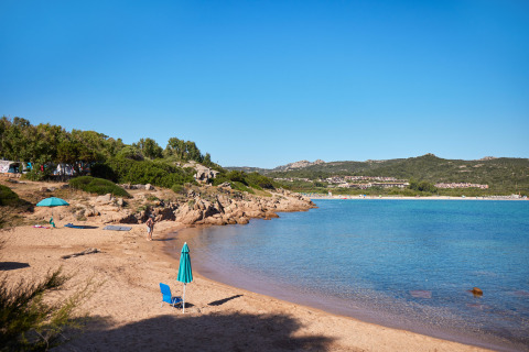 Sonniger Strand im Centro Vacanze Isuledda, Sardinien, Italien, mit ruhigem Wasser und blauem Himmel.