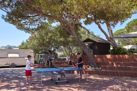 Niños juegan al ping-pong al aire libre bajo los árboles en Centro Vacanze Isuledda, Cerdeña, Italia.