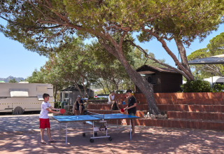 Bambini giocano a ping pong all'aperto sotto gli alberi al Centro Vacanze Isuledda in Sardegna, Italia.