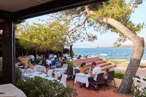 Buitenrestaurant met zeezicht aan Centro Vacanze Isuledda vakantiepark in Sardinië, Italië, met gasten.