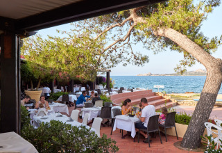 Buitenrestaurant met zeezicht aan Centro Vacanze Isuledda vakantiepark in Sardinië, Italië, met gasten.
