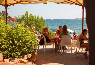 Mensen genieten op een zonnig terras aan zee bij Centro Vacanze Isuledda, Sardinië, Italië.