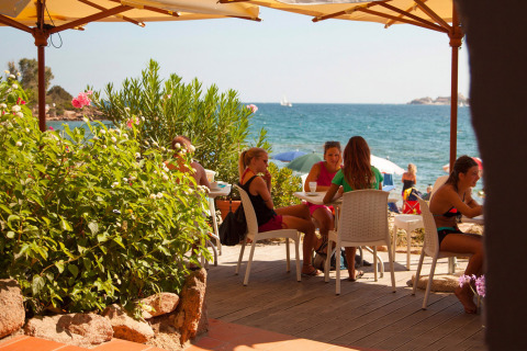 Personas relajándose en una terraza junto al mar en Centro Vacanze Isuledda, Cerdeña, Italia, al sol.