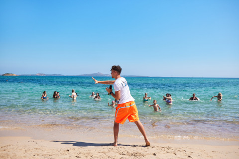 Activiteitenbegeleider in oranje short organiseert waterspelen op het strand bij Centro Vacanze Isuledda, Sardinië.