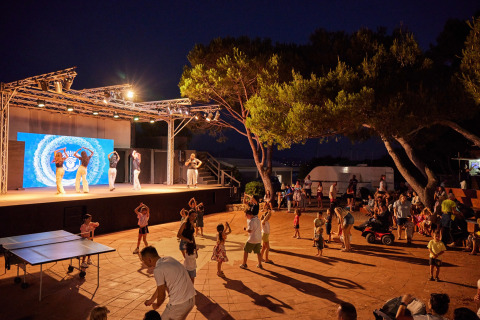 Soirée animée au Centro Vacanze Isuledda, Sardaigne, avec danseurs sur scène et vacanciers devant.