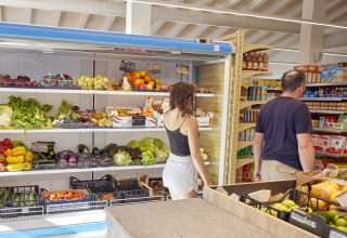 Two people shopping for fresh produce and groceries in a small supermarket at a Sardinia, Italy holiday park.