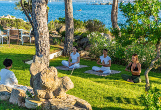 A group of people meditate on grass by the sea at Centro Vacanze Isuledda holiday park, Sardinia, Italy.