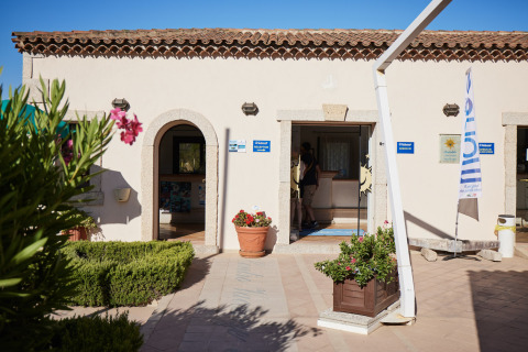 Ingang van Centro Vacanze Isuledda vakantiepark met receptie, bloemen en vlag, Sardinië, Italië.