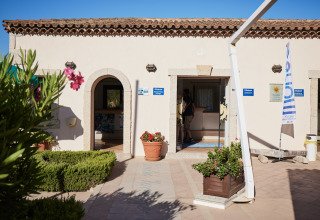 Ingresso del Centro Vacanze Isuledda con reception, fiori in vaso e bandiera, Sardegna, Italia.