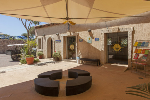 Indgang til Centro Vacanze Isuledda feriepark i Sardinien med moderne udendørs siddepladser og solskærm.