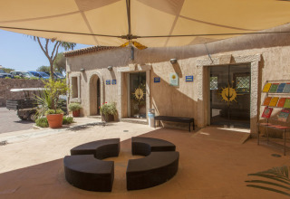 Indgang til Centro Vacanze Isuledda feriepark i Sardinien med moderne udendørs siddepladser og solskærm.