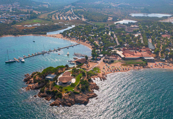 Vista aérea del Centro Vacanze Isuledda en Cerdeña, Italia, con playas, vegetación y puerto deportivo.