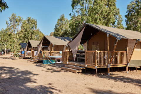 Safari tents with wooden decks at Centro Vacanze Isuledda holiday park in Sardinia, Italy, surrounded by trees.