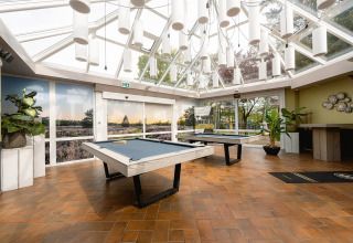 Lyst opholdsrum med billardborde og store vinduer i feriepark Ackersate i Gelderland, Holland.