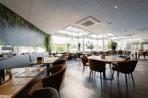 Lyst og moderne restaurantinteriør på Holiday Park Ackersate i Gelderland, Holland, med planter og træmøbler.