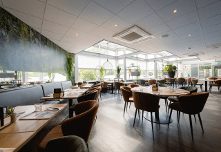 Lyst og moderne restaurantinteriør på Holiday Park Ackersate i Gelderland, Holland, med planter og træmøbler.