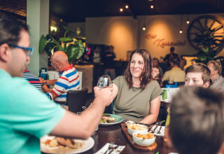 Familie isst zusammen im Restaurant im Holiday Park Ackersate, Gelderland, Niederlande, während sie lacht.