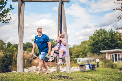 Hombre y niña se divierten en un columpio en Holiday Park Ackersate, un parque en Gelderland, Países Bajos, al aire libre.