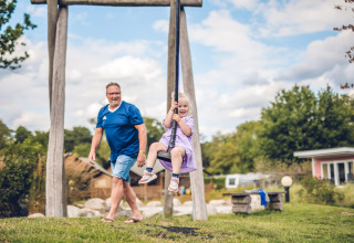 Mand og pige leger på en gynge i Holiday Park Ackersate, en feriepark i Gelderland, Holland, på en solskinsdag.