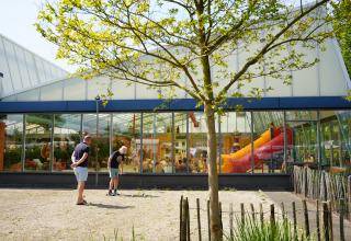 To personer spiller petanque udenfor en bygning med store vinduer og orange rutsjebane i Holiday Park Ackersate.