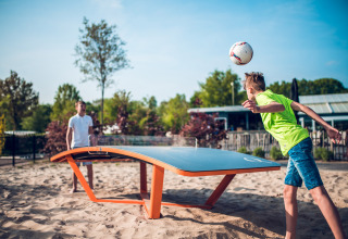 Two boys playing teqball on sand at Holiday Park Ackersate in Gelderland, Netherlands, under a sunny sky.
