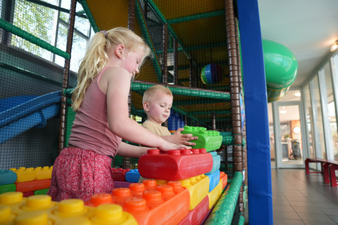 Dos niños juegan con bloques de construcción grandes en una zona de juegos cubierta en Holiday Park Ackersate, Gelderland.