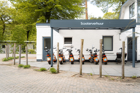 Alquiler de scooters frente a un edificio blanco en Holiday Park Ackersate, Gelderland, Países Bajos.