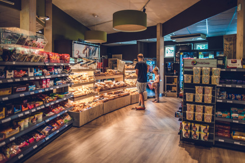 Supermercado en Holiday Park Ackersate, Gelderland, Países Bajos, con visitantes eligiendo panadería y snacks.