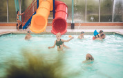 Børn leger og svømmer i en indendørs swimmingpool med rutsjebaner på Holiday Park Ackersate i Gelderland.