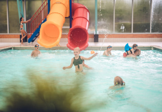 Børn leger og svømmer i en indendørs swimmingpool med rutsjebaner på Holiday Park Ackersate i Gelderland.